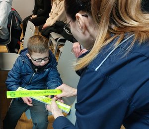 Polcijantka rozdaje elementy odblaskowe. Obok siedzi mały chłopiec