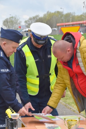 Dwóch funkcjonariuszy oraz opiekun uczniów spoglądają na dyplom przygotowany dla zwycięzcy. Dyplom leży na stoliku. Zdjęcie wykonane w miasteczku ruchu drogowego w Sędziszowie Małopolskim