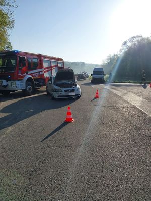 Miejsce zdarzenia drogowego. Na ulicy stoją pojazdy uczestniczące w kolizji. Oba są uszkodzone. Na drodze stoi także wóz strażacki.