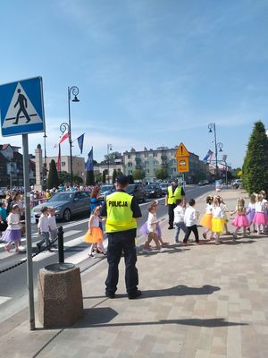 Policjant stoi w rejonie przejścia dla pieszych na którym znajdują się dzeci.