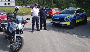 Dwóch policjantów stoi obok radiowozu i motocykla policyjnego