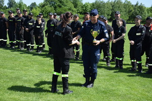 Policjant odbierający puchar od funkcjonariuszki straży pożarnej.