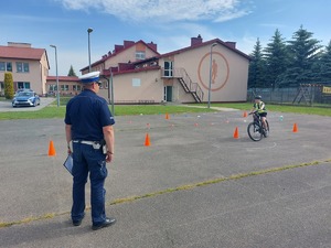 Policjant egzaminuje chłopca, który na rowerze wykonuje przejazd tzw osemką