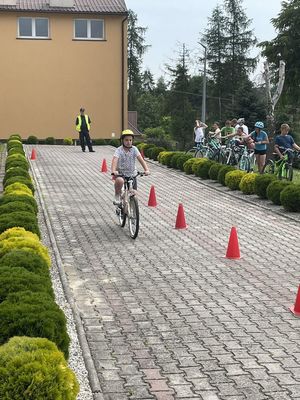 Na pierwszym planie widoczne dziecko na rowerze, które jedzie miedzy &quot;pachołkami&quot; a w oddali policjant