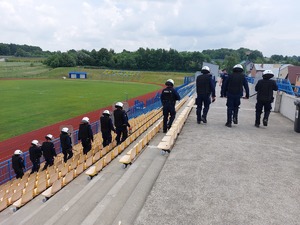 Policjanci tworzą tyralierę idą trybunami, które znajdują się na trybunach stadionu miejskiego w Ropczycach
