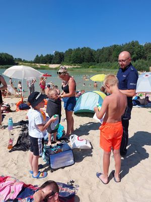 Policjant rozdaje na plaży ulotki dotyczące bezpiecznego wypoczynku