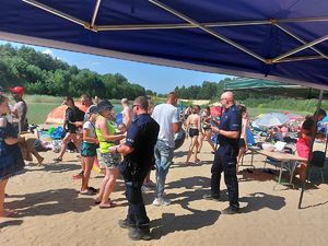 Dwóch policjantów rozdaje wśród plażowiczów ulotki dotyczące bezpieczeństwa.