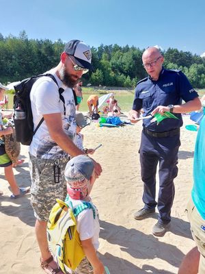 Policjant daje mężczyźnie z dwójką dzieci gadżety promujące bezpieczeństwo nad wodą