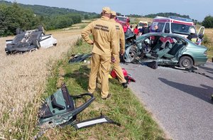 Po lewej stronie drogi widoczny pojazd, który dachował. Na ulicy widoczni strażacy oraz drugi pojazd uczestniczący w zdarzeniu.