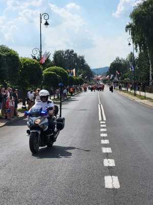 Policjant jadący na motocyklu, za nim przemarsz grupy ludzi