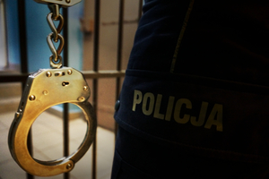policjant stojący przed PDOZ, w reku trzyma kajdanki