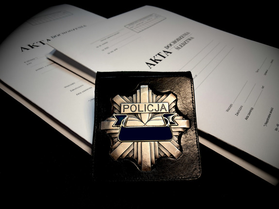 odznaka policyjna, w tle obwoluta akt postępowania