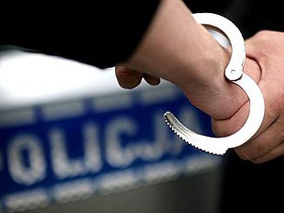 Kajdanki zakładane na ręce  w tle napis policja na bocznych drzwiach radiowozu